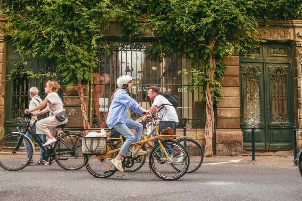 Urban cyclists riding past charming Paris architecture and greenery in daylight.